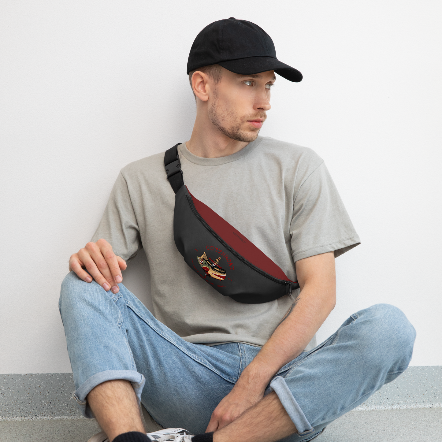 Man wearing a lost lure fly fishing bag/ Fanny pack. It has an American traditional style design with a cutthroat trout. It’s red and grey in color and has a pattern on the back of flies and trout.